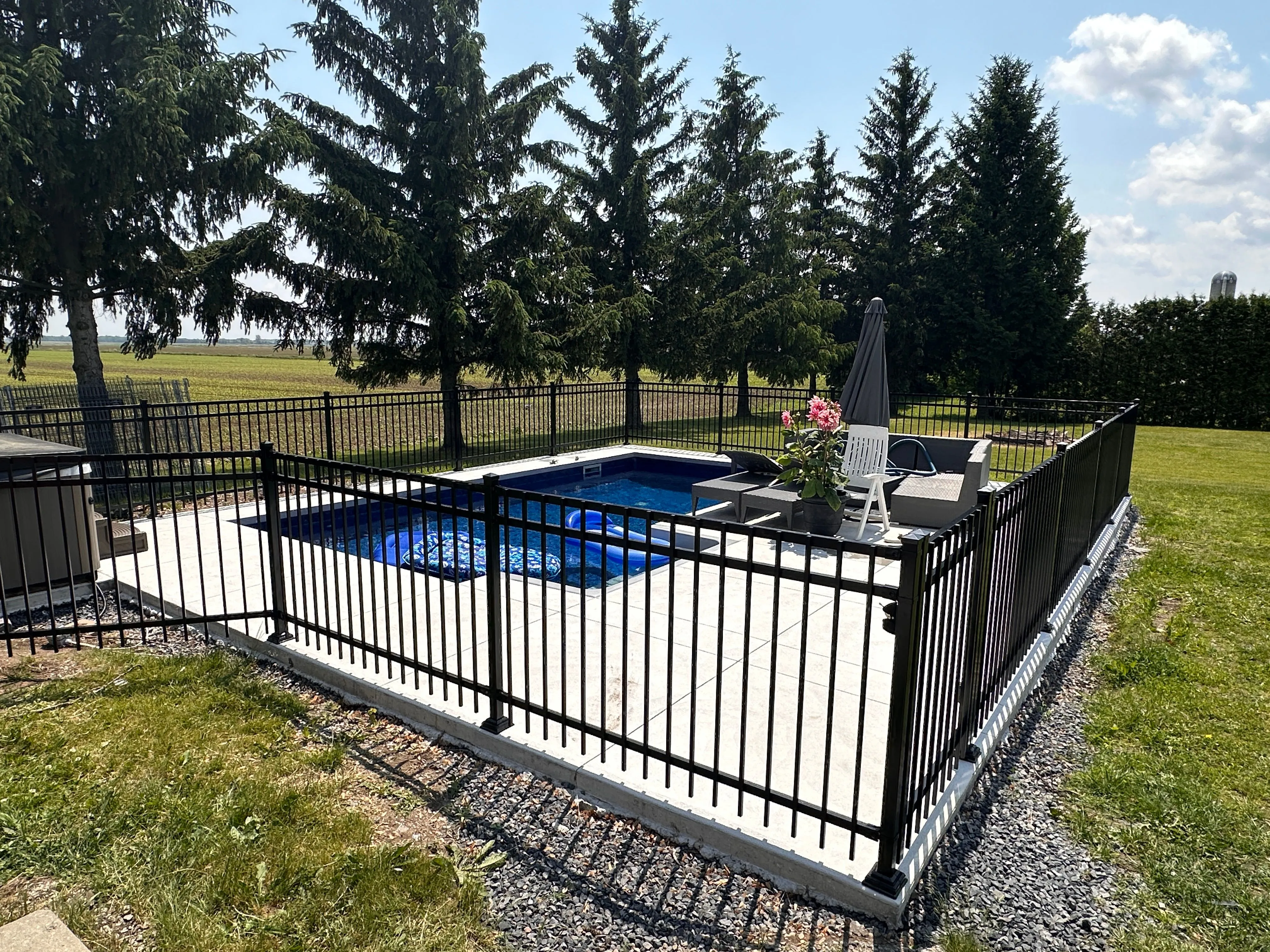 Clôture ornementale en aluminium autour d'une piscine avec conifères